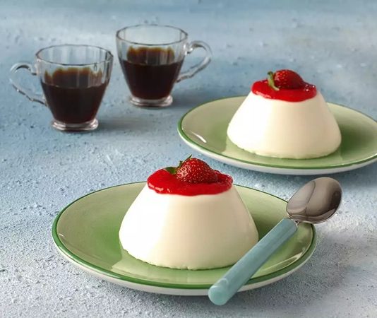 Panna Cotta Tatlı Dünyasında İtalyan Zarafetinin En Hafif Hâli İtalyan mutfağının en rafine tatlılarından biri olan panna cotta, hafif kıvamı, sütlü dokusu ve şık sunumuyla son yıllarda Türkiye’de de oldukça ilgi gören tatlılardan biri hâline geldi. Özellikle yaz aylarında serinletici etkisi nedeniyle tercih edilen bu özel tatlı, hem restoran hem de ev tariflerinde farklı versiyonlarla ortaya çıkıyor. Tatlının temelinde krema bulunması, ona kendine özgü yumuşaklığı kazandırırken, kullanılan vanilya ve meyveler tatlıya zarif bir aroma katıyor. Günümüzde modern pastacılık trendleri sayesinde daha geniş kitlelere ulaşan panna cotta, estetik sunumu ile de dikkat çekiyor. Konulu bir haber görseli.