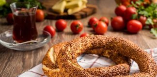 Simit ve Açma Kültürü Şehir Hayatında Değişmeyen Lezzetler Türkiye’de sokak lezzetleri denildiğinde akla gelen ilk tatlar arasında simit ve açma yer alır. Günün her saatinde ulaşılabilen bu iki hamur işi, yalnızca pratik bir atıştırmalık olmanın ötesinde, şehir yaşamının ritmini belirleyen önemli unsurlardan biri olarak görülür. Sabah işe yetişmeye çalışan bir memurun elinde, okul yolunda koşan bir öğrencinin çantasında ya da sahil kenarında çay eşliğinde tüketilen bu lezzetler, toplumsal hafızanın da güçlü bir parçasıdır. Konulu bir haber görseli.